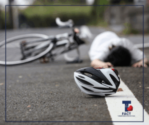 Casco de ciclista en el pavimento frente a una bicicleta accidentada y una persona caída en la carretera, ilustrando un accidente vial que puede causar trauma abdominal severo.