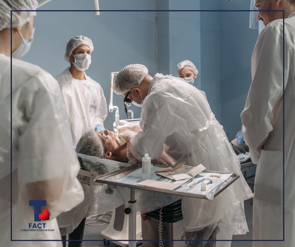 Equipo multidisciplinario de profesionales de la salud atiende a un paciente en un entorno clínico de trauma, utilizando equipo de protección personal y coordinando procedimientos médicos.